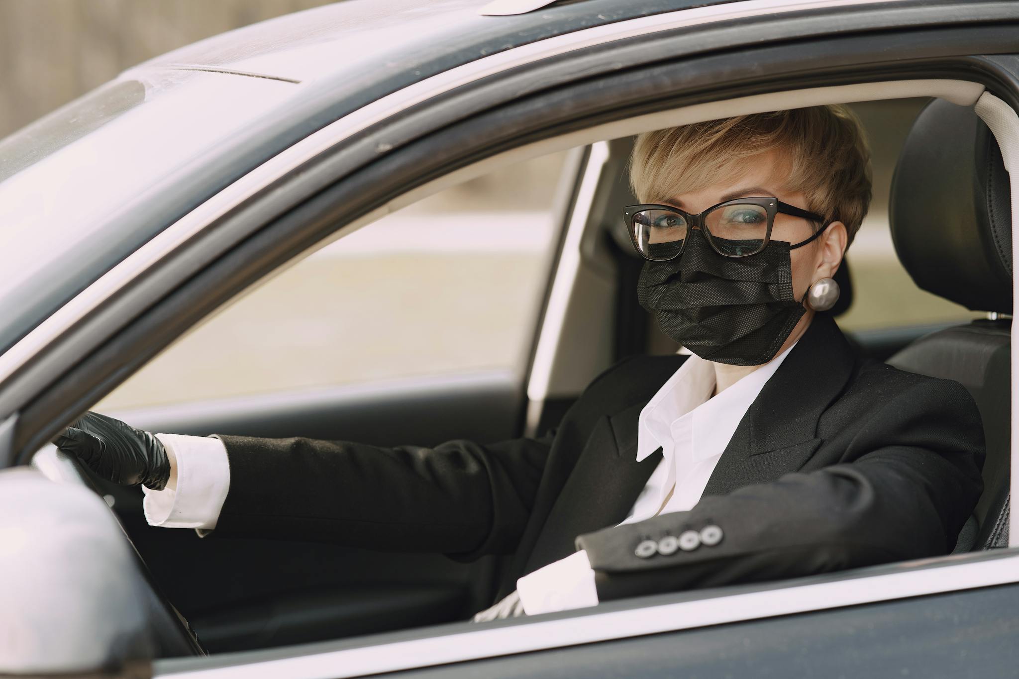 A woman wearing a mask and gloves drives a car, emphasizing safety during the pandemic.